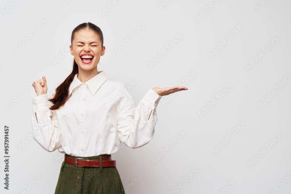 joyful woman, celebrating success with a big smile, wearing a white blouse and green pants, standing against a plain light grey background, conveying happiness and excitement joyful woman, celebrating success with a big smile, wearing a white blouse and green pants, standing against a plain light grey background, conveying happiness and excitement