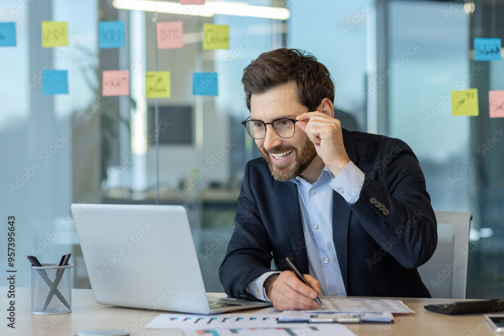 Smiling businessman using laptop in modern office setting Smiling businessman using laptop in modern office setting