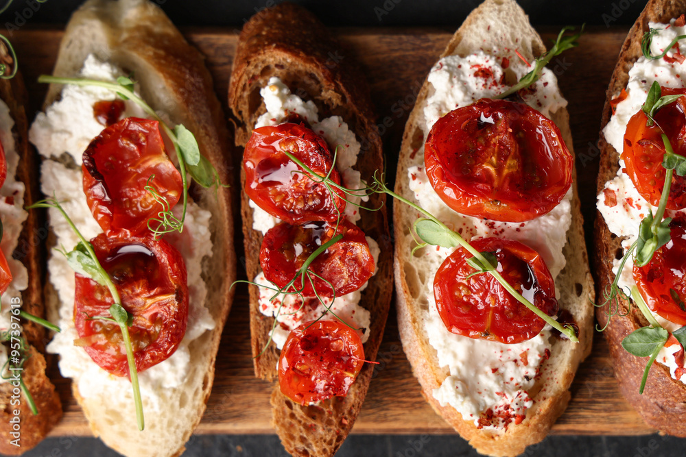 Wooden board of tasty tomato bruschetta with ricotta on black background, closeup