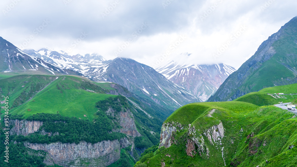 Fototapeta premium Panoramic view from the grassy hill on the Kazbek mountains and the green valley crossed