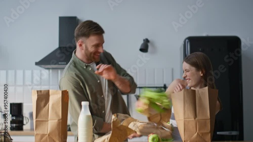 Laughing spouses unpacking groceries in home kitchen fooling together closeup.