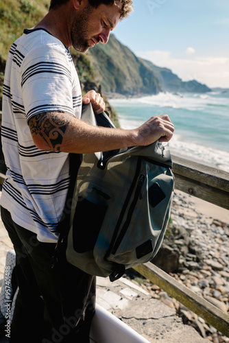 Man rummages through his belongings in a backpack near the beach photo