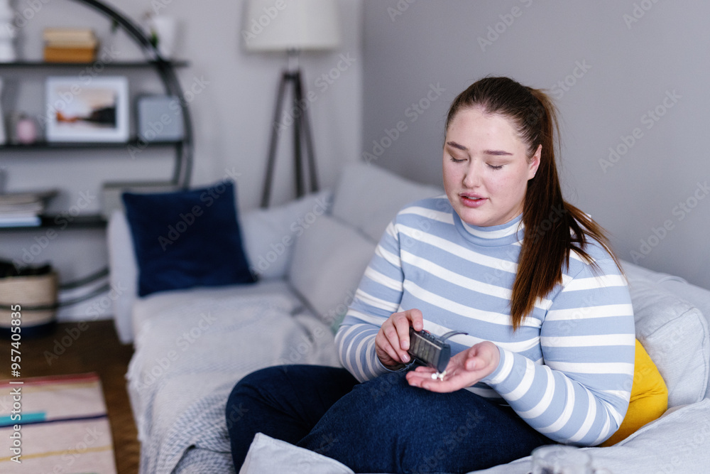 Plus size woman taking pills from pill organizer sitting on sofa Plus size woman taking pills from pill organizer sitting on sofa