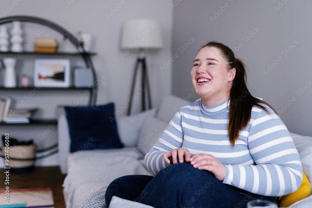 Young plus size woman laughing while sitting on sofa in living room Young plus size woman laughing while sitting on sofa in living room