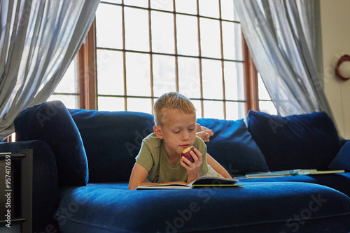 Little boy reading a book and eating an apple photo