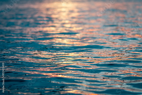 Blue water ripples reflecting orange and red sunset, foreground in focus