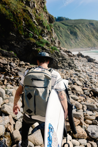 A surfer walks across a rocky beach searching for a surf spot photo