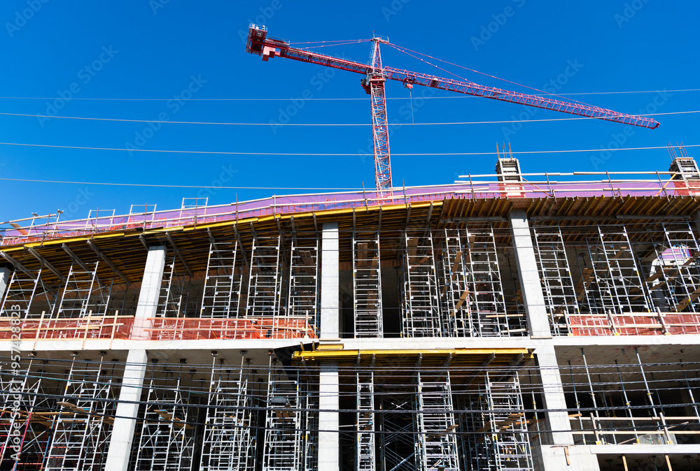 Naklejka premium Building and construction. Hoisting crane. Construction at building site with crane. Construction crane at building area. Construction site with building crane. Industrial area. Site inspection