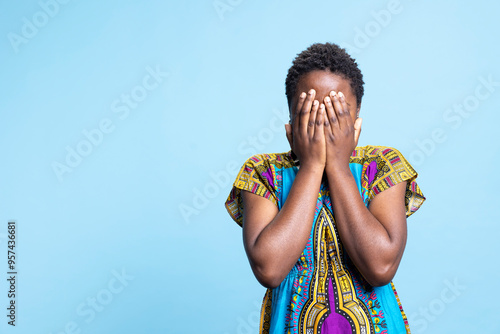 African american woman covering her eyes in shock and terror, person being afraid to look at something in studio. Young adult feeling unhappy and genuinely scared, serious anxiety. photo