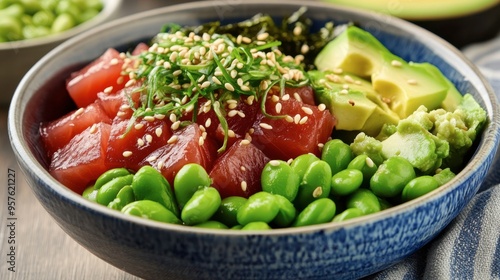 A colorful bowl of poke with tuna, avocado, edamame, seaweed salad, and a drizzle of soy sauce, garnished with sesame seeds.