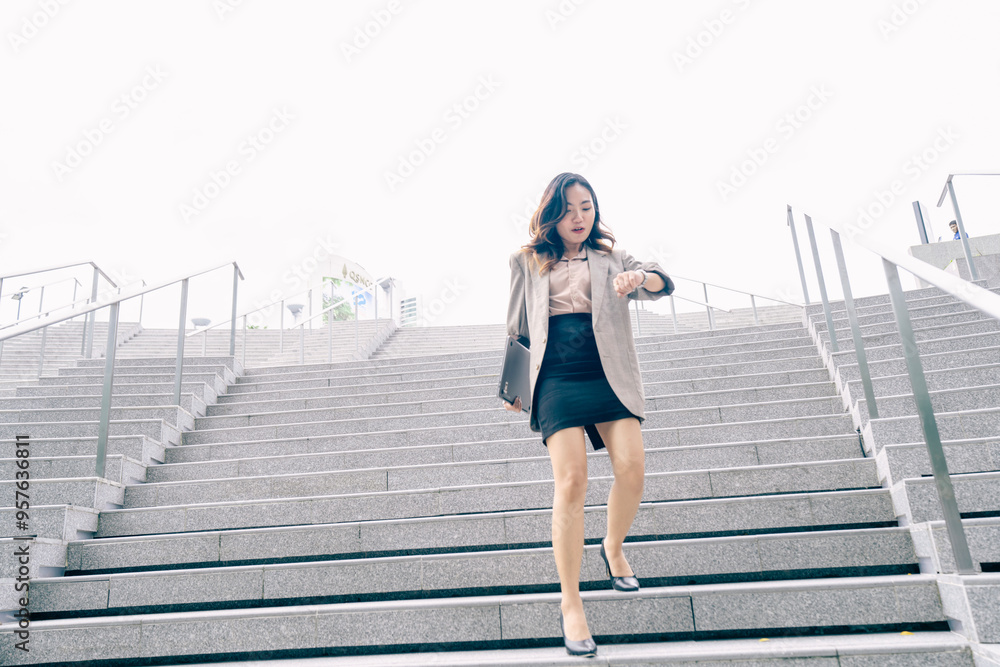 Obraz premium Asian business woman walking to work diligently and briskly in morning in a big city. female in a business suit, dressed in a smart suit, runs to work during rush hour in corridors and stairs.