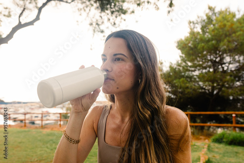 A fitness woman hydrates herself with water from a jerry can photo