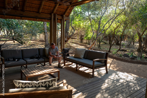 Male tourist relaxing in the sunlit lounge area of a safari camp.