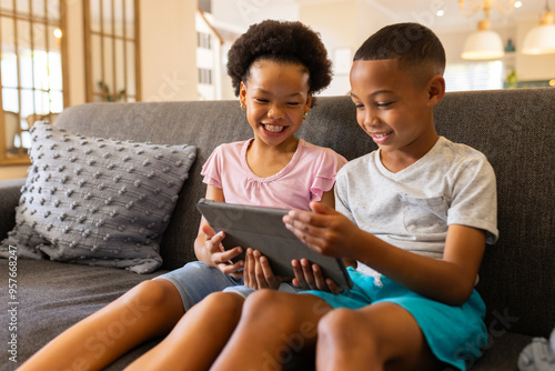 Sitting on couch, brother and sister using tablet and smiling, enjoying time together photo