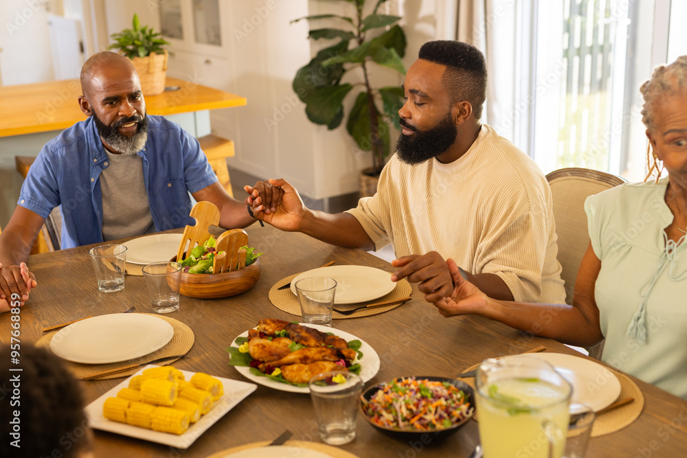 Fototapeta premium multigenerational family holding hands and praying before meal, gathered around dining table