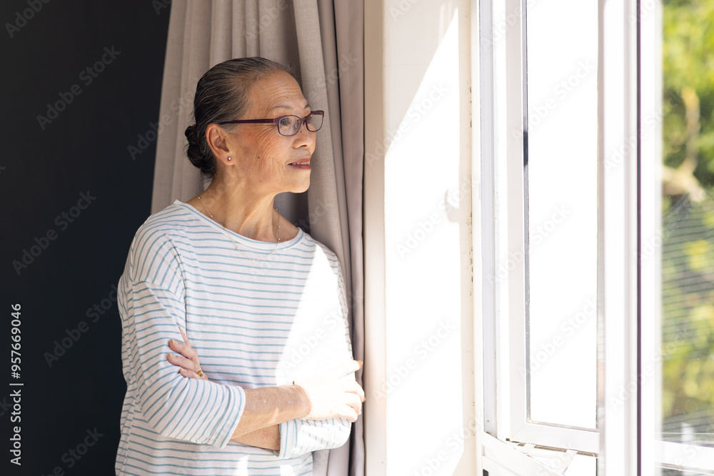 Looking out window, elderly asian woman in striped shirt enjoying sunlight indoors Looking out window, elderly asian woman in striped shirt enjoying sunlight indoors