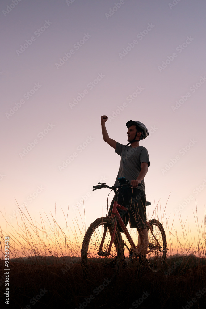 Mountain biker takes a break at dusk, raising his arm in victory. The scenic sunset and peaceful atmosphere capture a sense of accomplishment and a passion for outdoor adventure. Mountain biker takes a break at dusk, raising his arm in victory. The scenic sunset and peaceful atmosphere capture a sense of accomplishment and a passion for outdoor adventure.