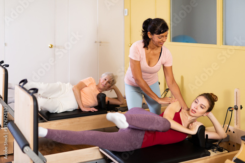 Friendly woman Pilates trainer helps to perform stretching exercises for a woman lying on a simulator bed in a fitness studio photo