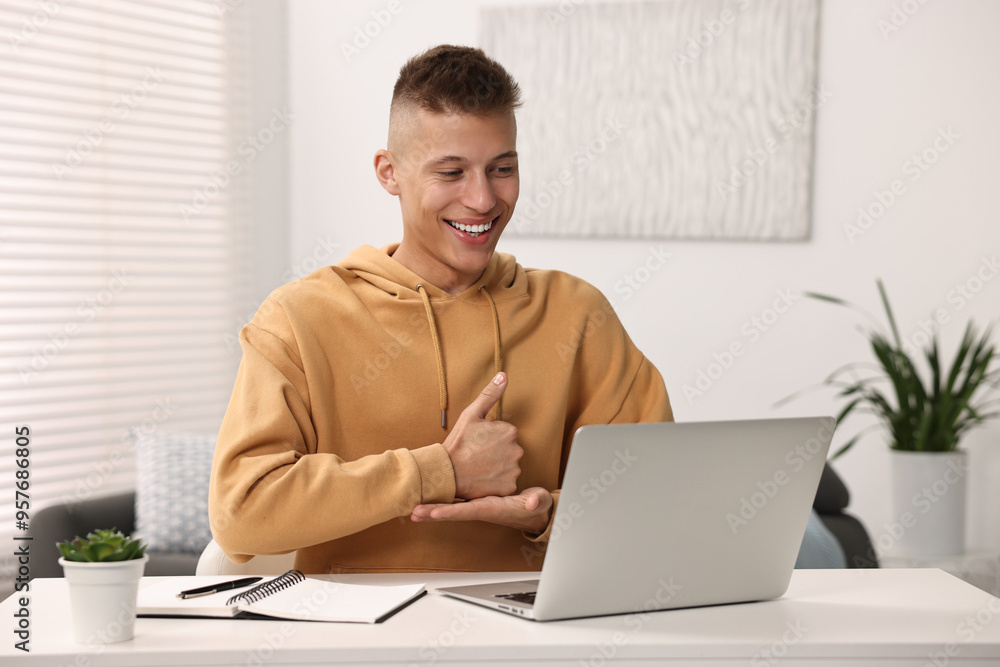 Fotografie Young man using sign language during video call indoors