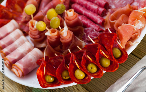 Appetizing cold cuts from Spanish ham, spicy dry-cured sausages and bacon with olives on white plate.. photo