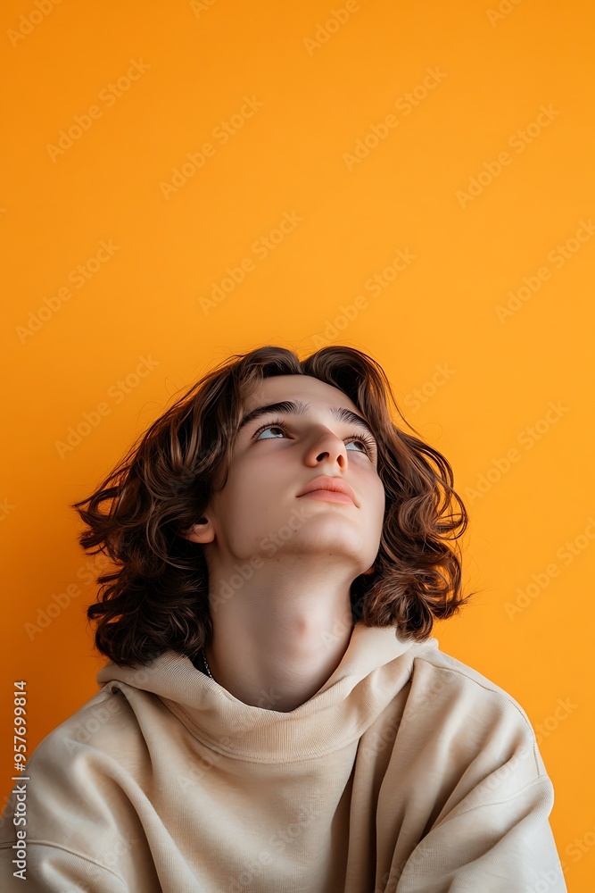 A teenager with a pensive expression, leaning against a vibrant orange isolated background, with enough blank space above their head for adding text A teenager with a pensive expression, leaning against a vibrant orange isolated background, with enough blank space above their head for adding text