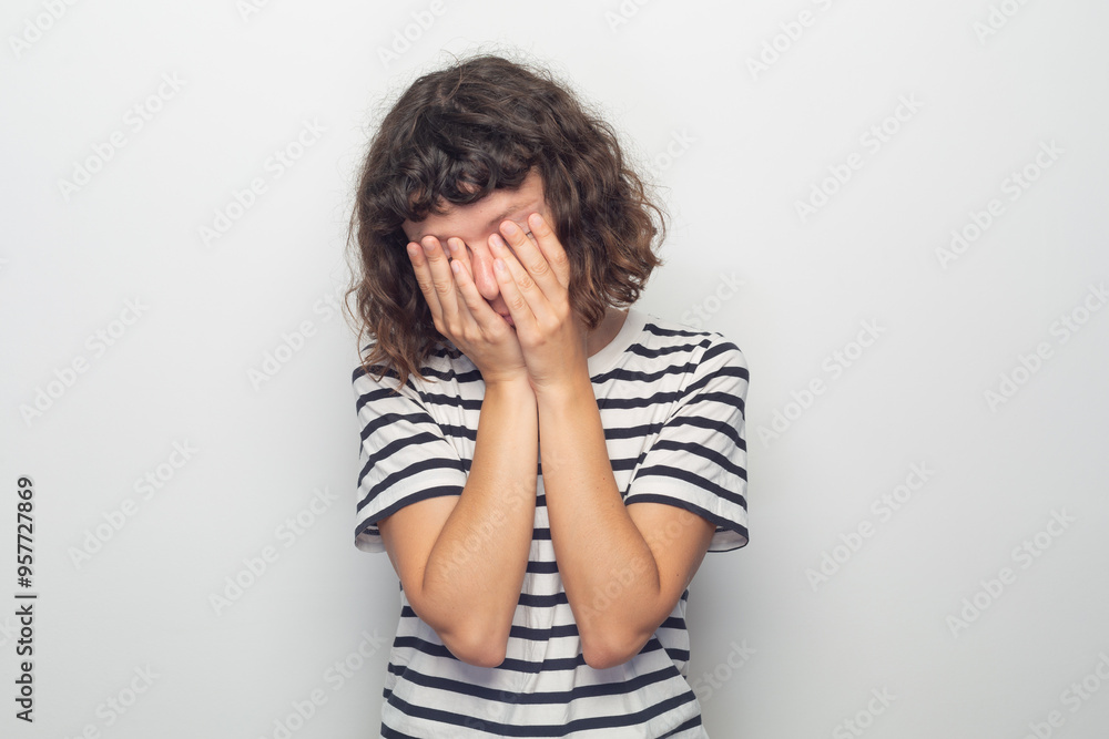 Curly-haired woman in striped shirt, covering her eyes with her hands Curly-haired woman in striped shirt, covering her eyes with her hands