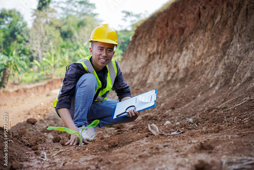 young male construction worker observing and examining the soil structure in the field and then recording it photo