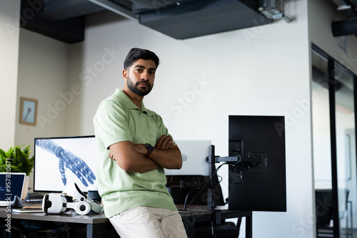 Indian man in office leaning on desk with robotic arm image on computer screen, copy space photo