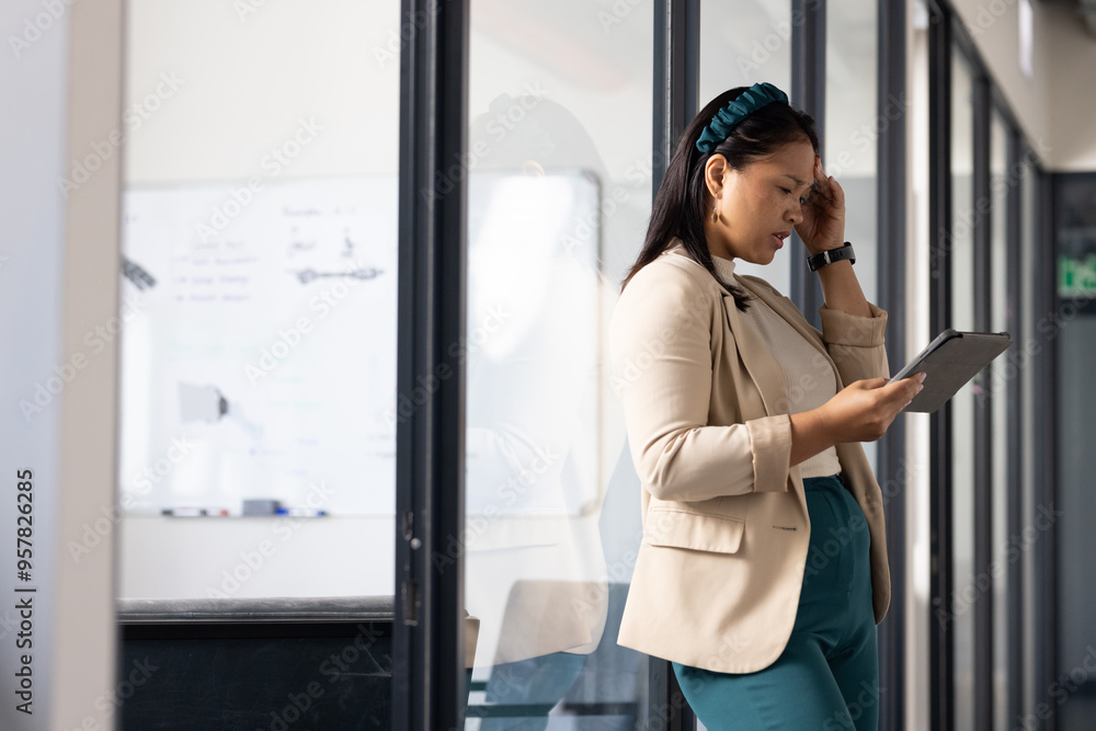 Using tablet, businesswoman standing in office hallway, concentrating on work, copy space Using tablet, businesswoman standing in office hallway, concentrating on work, copy space