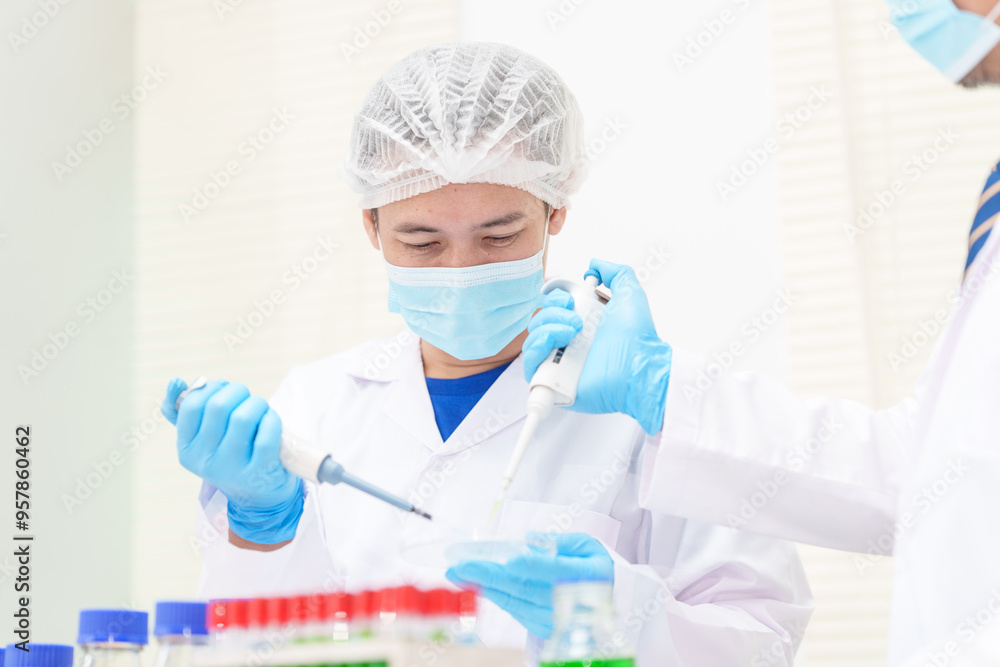 Two Asian scientists in lab coats sit at a table in a laboratory, examining samples through a microscope. The room is equipped with scientific tools, liquids, and chemistry materials. Two Asian scientists in lab coats sit at a table in a laboratory, examining samples through a microscope. The room is equipped with scientific tools, liquids, and chemistry materials.