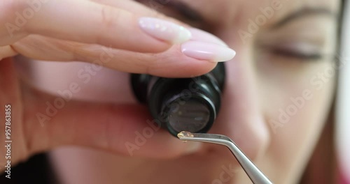 Woman examines small yellow gemstone with tweezers photo