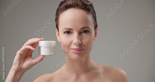 Beauty, health, cosmetics, anti-aging therapy and skin care concept - young beautiful brunette Caucasian woman holding a jar of moisturizer in her hands and looking at the camera