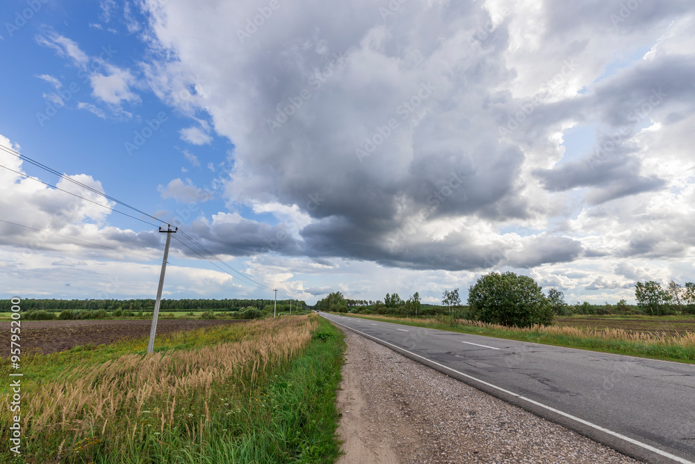 A road with a few trees in the background and a cloudy sky A road with a few trees in the background and a cloudy sky