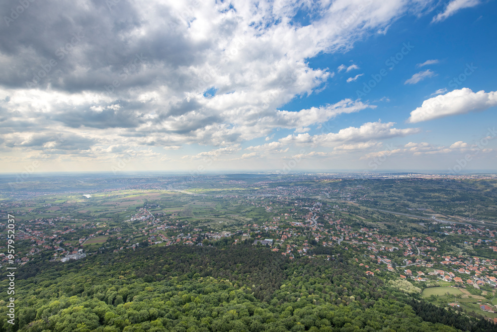 Obraz premium A city view with a cloudy sky and a green forest in the background