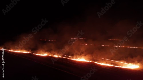 Raging fire at the dry grass meadow. Agricultural field fire burning. Night aerial footage of smoke and flame. Firefighters emergency response. Ecological catastrophe and environmental hazard.