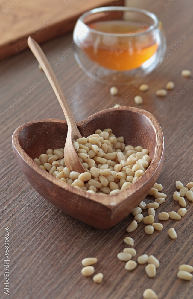 Natural pine nuts in heart shape bowl. Wooden dishes and furniture in kitchen. Fresh clear honey in glass bowl. Healthy products. Natural pine nuts in heart shape bowl. Wooden dishes and furniture in kitchen. Fresh clear honey in glass bowl. Healthy products.