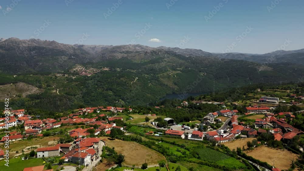 Aerial - Picturesque Salamonde village with red rooftops, lush fields, and dramatic Gerês mountain backdrop in Portugal Aerial - Picturesque Salamonde village with red rooftops, lush fields, and dramatic Gerês mountain backdrop in Portugal