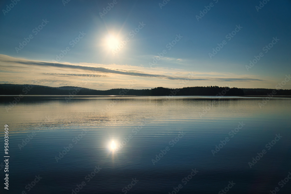 Sunrise over a Swedish lake with mirror-smooth water in front of trees on the shore Sunrise over a Swedish lake with mirror-smooth water in front of trees on the shore