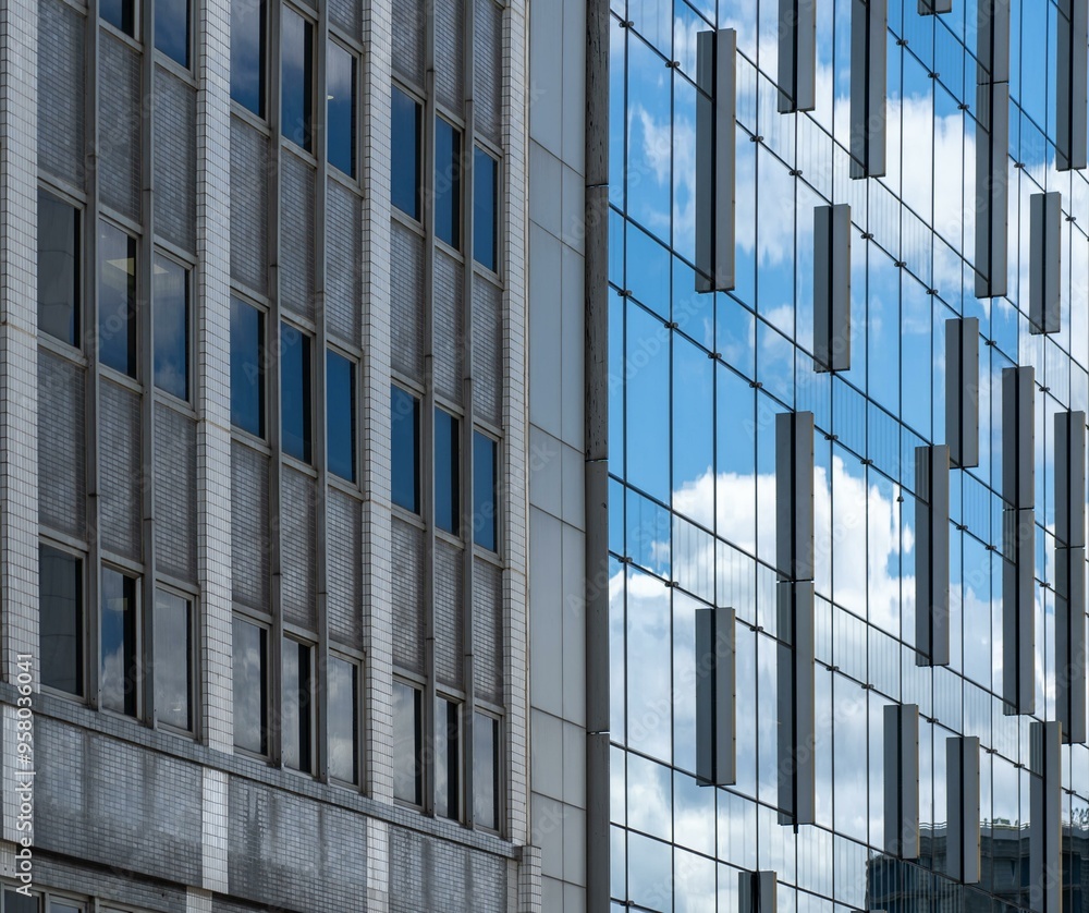 Two buildings, one with a tiled facade, the other glass, with reflective sky and clouds. Two buildings, one with a tiled facade, the other glass, with reflective sky and clouds.