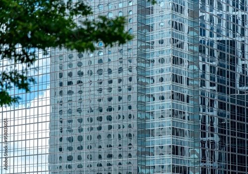 A modern skyscraper in Hong Kong, China, with a grid of windows reflecting the blue sky and clouds.