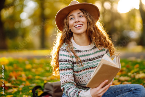 A young woman enjoys reading by a serene lake surrounded by autumn leaves in a park during sunset. Relaxation, enjoying, solitude with nature. photo