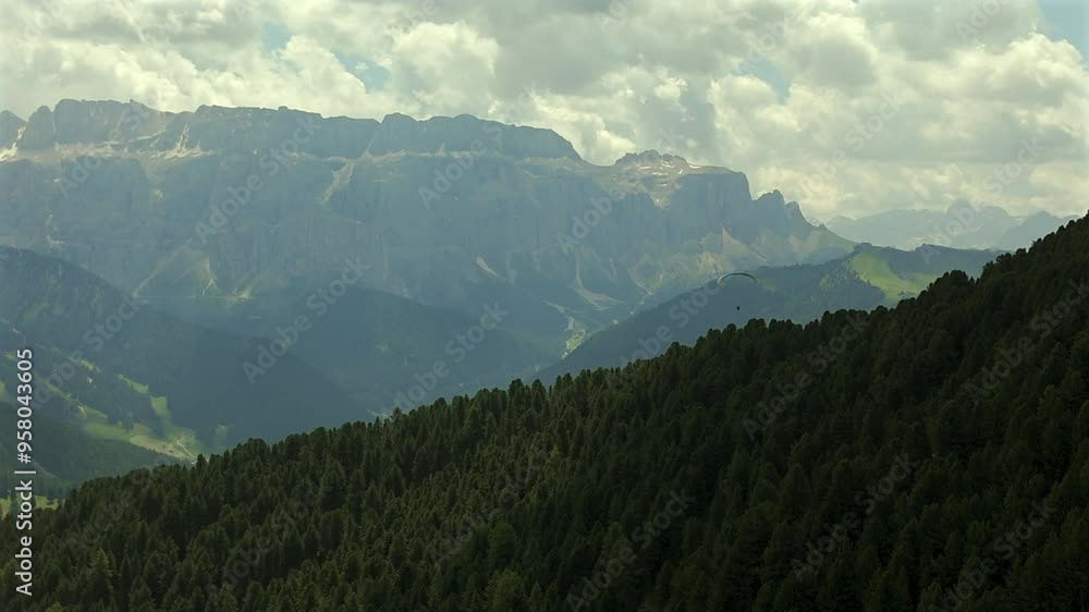 A paraglider soars above dense forested hills with a stunning backdrop of towering mountains in the Dolomites, showcasing the region’s natural beauty and adventure opportunities. A paraglider soars above dense forested hills with a stunning backdrop of towering mountains in the Dolomites, showcasing the region’s natural beauty and adventure opportunities.