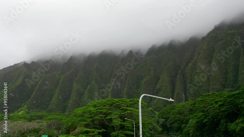 Drone ascends to mist-covered Koolau mountain ridges with dense green vegetation, mist adds a layer of mystery to the tranquil and untouched natural environment above the H-1 Highway photo