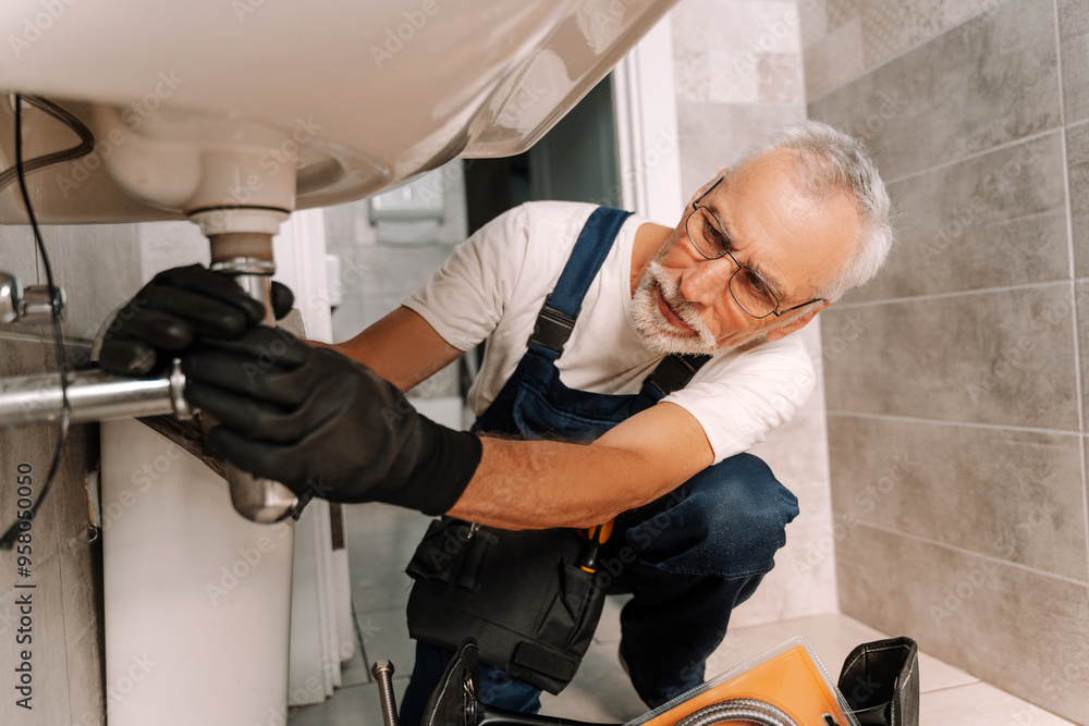 Senior plumber wearing gloves repairing sink pipe in bathroom Senior plumber wearing gloves repairing sink pipe in bathroom
