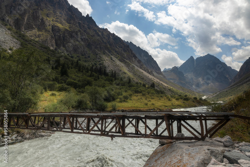 A small unsteady bridge over the rapid river in the mountains of Ala Archa National park valley photo