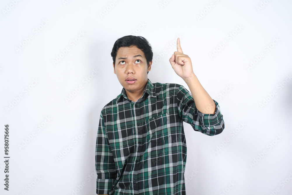 puzzled young asian man pointing above and looking up with wondering face and clueless expression isolated on white background puzzled young asian man pointing above and looking up with wondering face and clueless expression isolated on white background