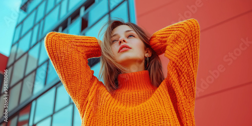 Confident woman in bright orange sweater against modern urban glass architecture photo