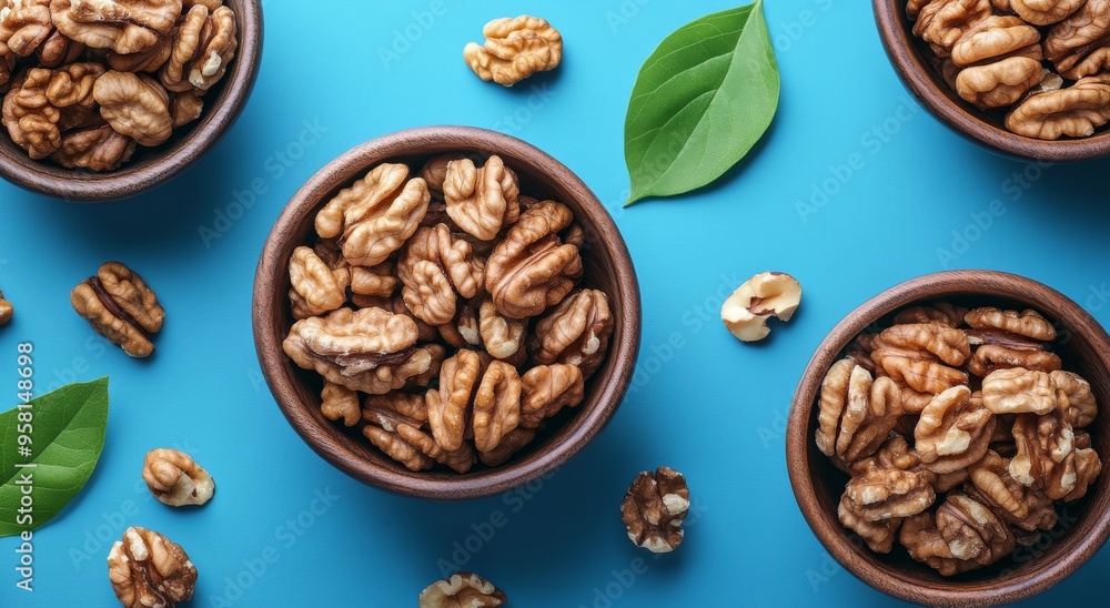 Fresh walnuts arranged in bowls with green leaves on a textured blue background Fresh walnuts arranged in bowls with green leaves on a textured blue background