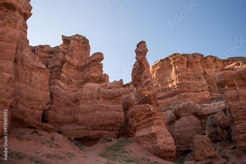 the grandeur of towering red sandstone cliffs against a clear azure sky, a serene, untouched wilderness in late summer or early fall due to the warm lighting.