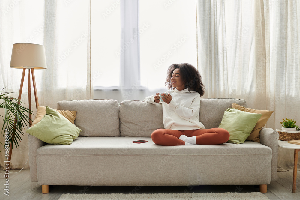 A young woman with curly hair sips her drink while lounging comfortably at home in cozy attire. A young woman with curly hair sips her drink while lounging comfortably at home in cozy attire.